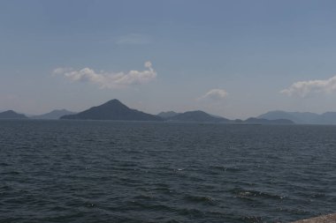 Bu Hiroşima Körfezi 'nin bir görüntüsü. Dalgalar, tuzlu suyun dalgalı tepelere ulaşmasıyla güzel ve sakin görünüyor. Güzel mavi Japon gökyüzünün içinde beyaz bulutlar var..