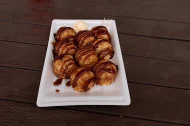 Tatlı ve lezzetli soslu bu altın kahverengi toplar Takoyaki 'dir. Onlar Japonya 'nın temel taşlarıdır. Burada beyaz bir tabakta servis edilirken ve yanında mayonez parçacıkları ile görülürler..