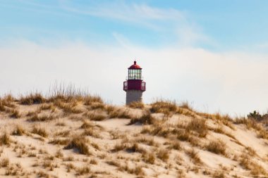 Majestic Cape May Deniz Feneri kumlu kum tepelerinin tepesinde, parlak mavi bir gökyüzüne karşı dimdik ayakta duruyor. Huzurlu bir sahil manzarası.