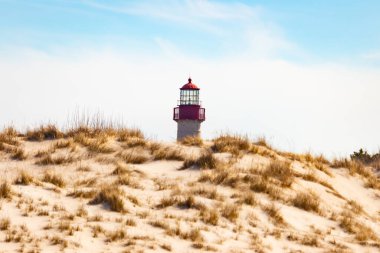 Majestic Cape May Deniz Feneri kumlu kum tepelerinin tepesinde, parlak mavi bir gökyüzüne karşı dimdik ayakta duruyor. Huzurlu bir sahil manzarası.