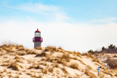 Majestic Cape May Deniz Feneri kumlu kum tepelerinin tepesinde, parlak mavi bir gökyüzüne karşı dimdik ayakta duruyor. Huzurlu bir sahil manzarası.