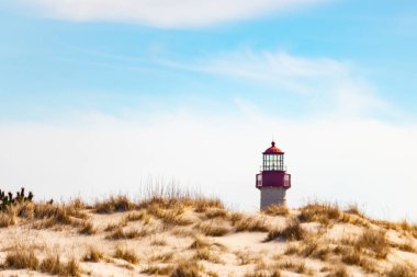 Majestic Cape May Deniz Feneri kumlu kum tepelerinin tepesinde, parlak mavi bir gökyüzüne karşı dimdik ayakta duruyor. Huzurlu bir sahil manzarası.
