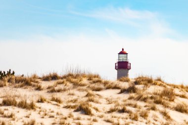 Majestic Cape May Deniz Feneri kumlu kum tepelerinin tepesinde, parlak mavi bir gökyüzüne karşı dimdik ayakta duruyor. Huzurlu bir sahil manzarası.