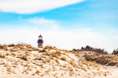 Majestic Cape May Deniz Feneri kumlu kum tepelerinin tepesinde, parlak mavi bir gökyüzüne karşı dimdik ayakta duruyor. Huzurlu bir sahil manzarası.