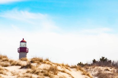 Majestic Cape May Deniz Feneri kumlu kum tepelerinin tepesinde, parlak mavi bir gökyüzüne karşı dimdik ayakta duruyor. Huzurlu bir sahil manzarası.
