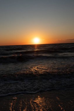 Güneşin ufukta battığı nefes kesici bir okyanus gün batımı dalgalanan mavi suya sıcak bir altın parıltı saçıyor. Huzurlu ve resimli sahil manzarası.