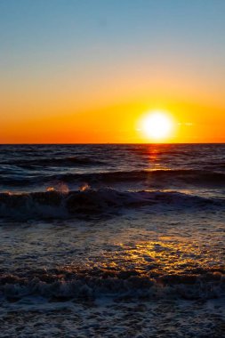 Güneşin ufukta battığı nefes kesici bir okyanus gün batımı dalgalanan mavi suya sıcak bir altın parıltı saçıyor. Huzurlu ve resimli sahil manzarası.