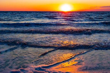 Güneşin ufukta battığı nefes kesici bir okyanus gün batımı dalgalanan mavi suya sıcak bir altın parıltı saçıyor. Huzurlu ve resimli sahil manzarası.