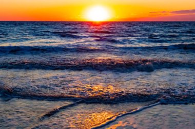 Güneşin ufukta battığı nefes kesici bir okyanus gün batımı dalgalanan mavi suya sıcak bir altın parıltı saçıyor. Huzurlu ve resimli sahil manzarası.