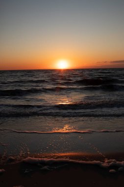 Güneşin ufukta battığı nefes kesici bir okyanus gün batımı dalgalanan mavi suya sıcak bir altın parıltı saçıyor. Huzurlu ve resimli sahil manzarası.
