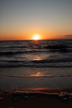 Güneşin ufukta battığı nefes kesici bir okyanus gün batımı dalgalanan mavi suya sıcak bir altın parıltı saçıyor. Huzurlu ve resimli sahil manzarası.