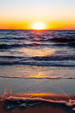 Güneşin ufukta battığı nefes kesici bir okyanus gün batımı dalgalanan mavi suya sıcak bir altın parıltı saçıyor. Huzurlu ve resimli sahil manzarası.
