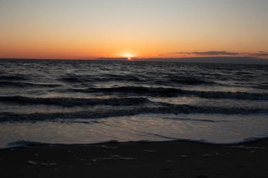 Güneşin ufukta battığı nefes kesici bir okyanus gün batımı dalgalanan mavi suya sıcak bir altın parıltı saçıyor. Huzurlu ve resimli sahil manzarası.