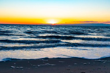 Güneşin ufukta battığı nefes kesici bir okyanus gün batımı dalgalanan mavi suya sıcak bir altın parıltı saçıyor. Huzurlu ve resimli sahil manzarası.