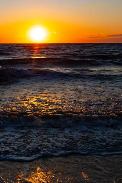 Güneşin ufukta battığı nefes kesici bir okyanus gün batımı dalgalanan mavi suya sıcak bir altın parıltı saçıyor. Huzurlu ve resimli sahil manzarası.