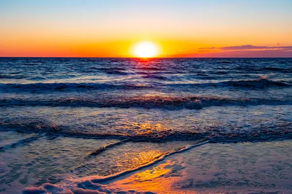 Güneşin ufukta battığı nefes kesici bir okyanus gün batımı dalgalanan mavi suya sıcak bir altın parıltı saçıyor. Huzurlu ve resimli sahil manzarası.