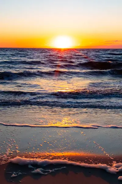 Güneşin ufukta battığı nefes kesici bir okyanus gün batımı dalgalanan mavi suya sıcak bir altın parıltı saçıyor. Huzurlu ve resimli sahil manzarası.