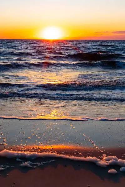 Güneşin ufukta battığı nefes kesici bir okyanus gün batımı dalgalanan mavi suya sıcak bir altın parıltı saçıyor. Huzurlu ve resimli sahil manzarası.