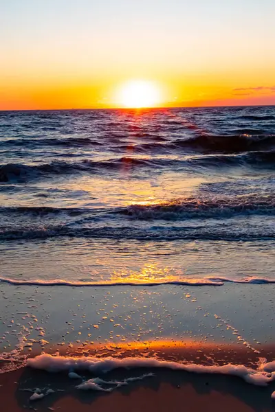 Güneşin ufukta battığı nefes kesici bir okyanus gün batımı dalgalanan mavi suya sıcak bir altın parıltı saçıyor. Huzurlu ve resimli sahil manzarası.
