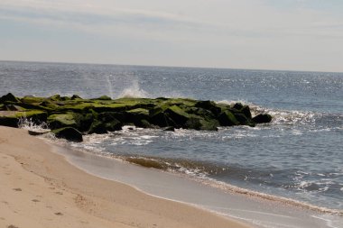 Bu, suya uzanan bir iskelenin resmi. Dalgalar etrafa köpük saçıyor. Körfezden çıkan büyük siyah kayaların üzerinde yeşil yosun yetişiyor..