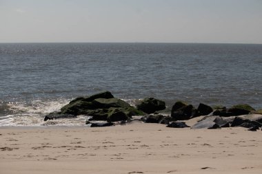 Bu, suya uzanan bir iskelenin resmi. Dalgalar etrafa köpük saçıyor. Körfezden çıkan büyük siyah kayaların üzerinde yeşil yosun yetişiyor..