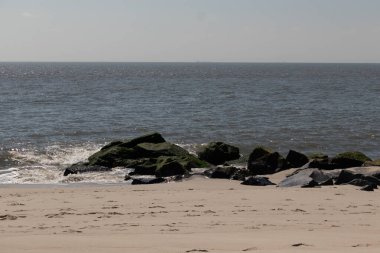 Bu, suya uzanan bir iskelenin resmi. Dalgalar etrafa köpük saçıyor. Körfezden çıkan büyük siyah kayaların üzerinde yeşil yosun yetişiyor..
