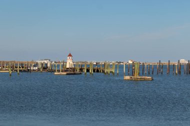 Bu çok güzel bir kıyı şeridi görüntüsü. Yerleşen suyun karayla buluşmasını gösteriyor. Yumuşak su çok sakin ve açık mavi gökyüzünü yansıtıyor. Arkasında bir liman var, ahşap rıhtımı gösteriyor..