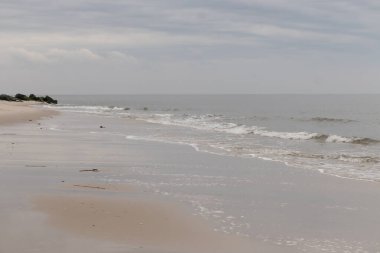 Bu plajın güzel bir gününün görüntüsü. Dalgaların yumuşak akıntıları kıyıya vurmaya geliyor, her geçişte kumu dışarı taşıyor. Bulutlar gökyüzüne yayıldı..