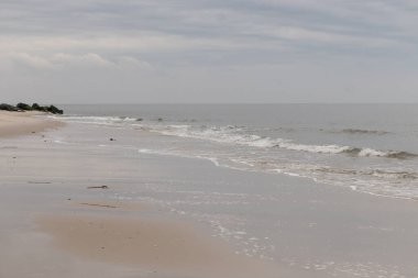 Bu plajın güzel bir gününün görüntüsü. Dalgaların yumuşak akıntıları kıyıya vurmaya geliyor, her geçişte kumu dışarı taşıyor. Bulutlar gökyüzüne yayıldı..