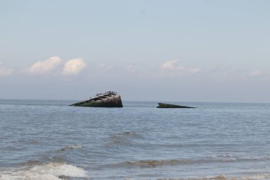 Bu, New Jersey Burnu 'ndaki Sunset sahilindeki batık geminin resmi. Okyanustan çıkan paslı metal gövde. Kahverengi tekne sahil kuşları için bir yaşam alanı değildir. Dalgaların her çarpışmada sahili öptüğü görülüyor..