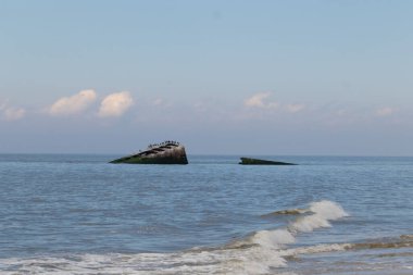 Bu, New Jersey Burnu 'ndaki Sunset sahilindeki batık geminin resmi. Okyanustan çıkan paslı metal gövde. Kahverengi tekne sahil kuşları için bir yaşam alanı değildir. Dalgaların her çarpışmada sahili öptüğü görülüyor..