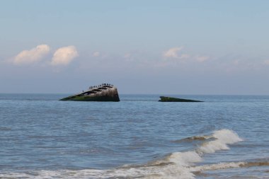 Bu, New Jersey Burnu 'ndaki Sunset sahilindeki batık geminin resmi. Okyanustan çıkan paslı metal gövde. Kahverengi tekne sahil kuşları için bir yaşam alanı değildir. Dalgaların her çarpışmada sahili öptüğü görülüyor..