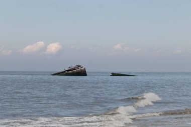 Bu, New Jersey Burnu 'ndaki Sunset sahilindeki batık geminin resmi. Okyanustan çıkan paslı metal gövde. Kahverengi tekne sahil kuşları için bir yaşam alanı değildir. Dalgaların her çarpışmada sahili öptüğü görülüyor..