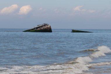 Bu, New Jersey Burnu 'ndaki Sunset sahilindeki batık geminin resmi. Okyanustan çıkan paslı metal gövde. Kahverengi tekne sahil kuşları için bir yaşam alanı değildir. Dalgaların her çarpışmada sahili öptüğü görülüyor..