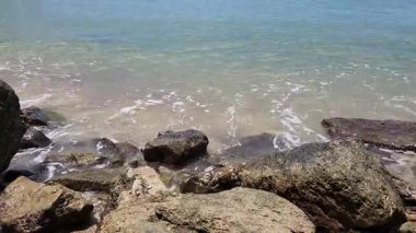 Deniz dalgalarının beyaz köpüğü sahildeki kayalara çarpıyor.