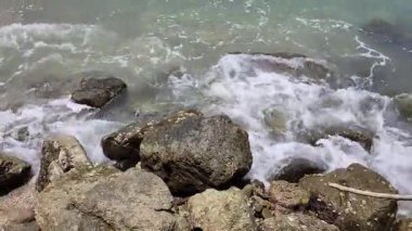 Denizin dalgalarından gelen beyaz köpük sahildeki kayalara çarpıyor.