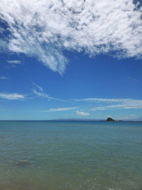 Deniz manzarası ve sakin suları ve mavi gökyüzünde dokulu bulutları olan küçük bir ada. 03