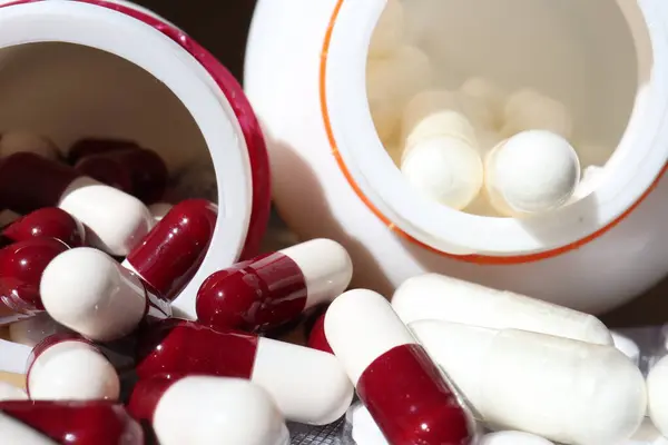 Beyaz ve kırmızı kapsüller beyaz plastik şişeden dökülmüş. Küresel sağlık hizmeti kavramı. Antibiyotik ilaç direnci. Antimikrobik kapsül hapları. İlaç sanayisi. Eczane. 