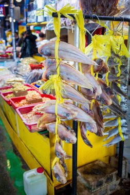 Dried fish hanging on a yellow rope. There are several fish hanging from the stand at seafood market clipart