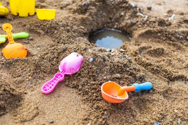 Pembe ve turuncu plastik kaşık kumun üzerinde. Yakınlarda başka plastik kaşıklar ve sarı bir kova var.