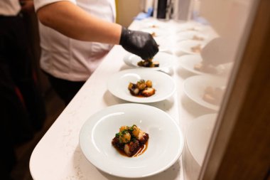 Şef tezgahta birkaç tabak yemek hazırlıyor. Tabaklar beyaz ve üzerinde çeşitli yemekler var.