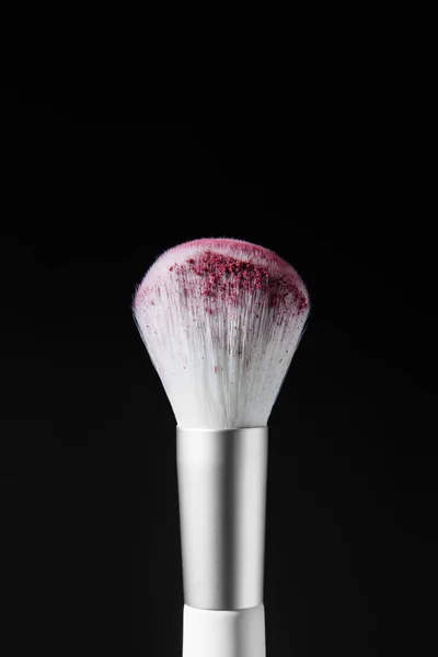 Large white brush with pink makeup powder. Advertising photo. On a black background.