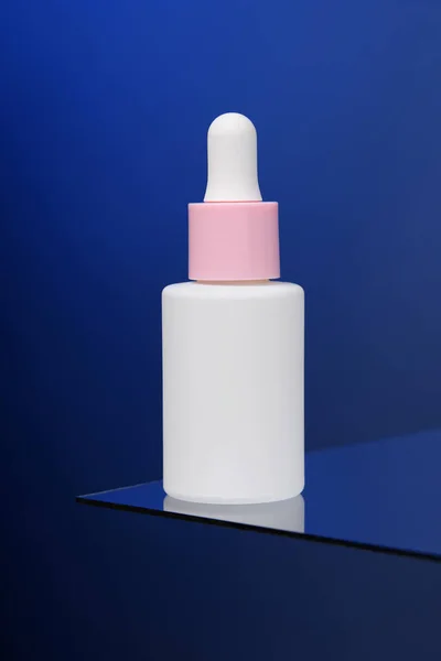 stock image In the blue background, a bottle of serum stands on glass.  Vertical advertising photo of cosmetics. Mockup. Template. 