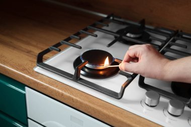 Bir adam gaz sobasını kibritle yakıyor. Gaz pişirmek tehlikelidir. Bütçe açığı. Mutfağa. Kahverengi masa üstü.