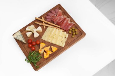 Peynir tahtası beyaz masada. Farklı peynir türleri, kırmızı biber, jamon, sosis, zeytin, domates, mikroçerez, bıçak, ekmek çubuğu. Atıştırmalık Peynir parçaları..