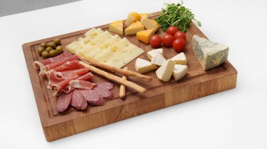 Peynir tahtası beyaz masada. Farklı peynir türleri, kırmızı biber, jamon, sosis, zeytin, domates, mikroçerez, bıçak, ekmek çubuğu. Atıştırmalık Peynir parçaları..