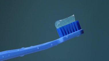 Islak, bayraklarla kaplı, mavi arka planda diş macunlu mavi plastik bir diş fırçası. Işığın etkisi. Ağız boşluğuna dikkat et..