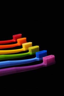 Siyah arka planda çok renkli plastik diş fırçaları. Diş hekimliği afişi. Gökkuşağının renkleri.
