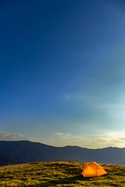 Dağın tepesinde gün batımı. Bir dağ manzarasının arka planında bir çadır.
