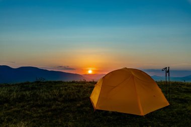 Dağın tepesinde gün batımı. Bir dağ manzarasının arka planında bir çadır.